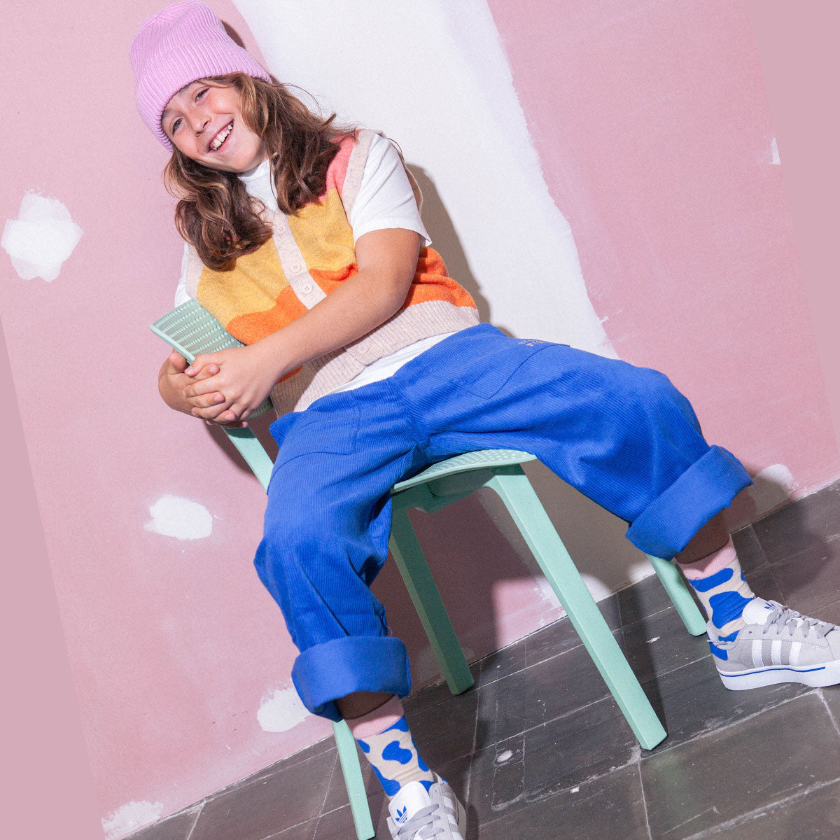 Child sitting on a stool against a pink wall with white paint splashes