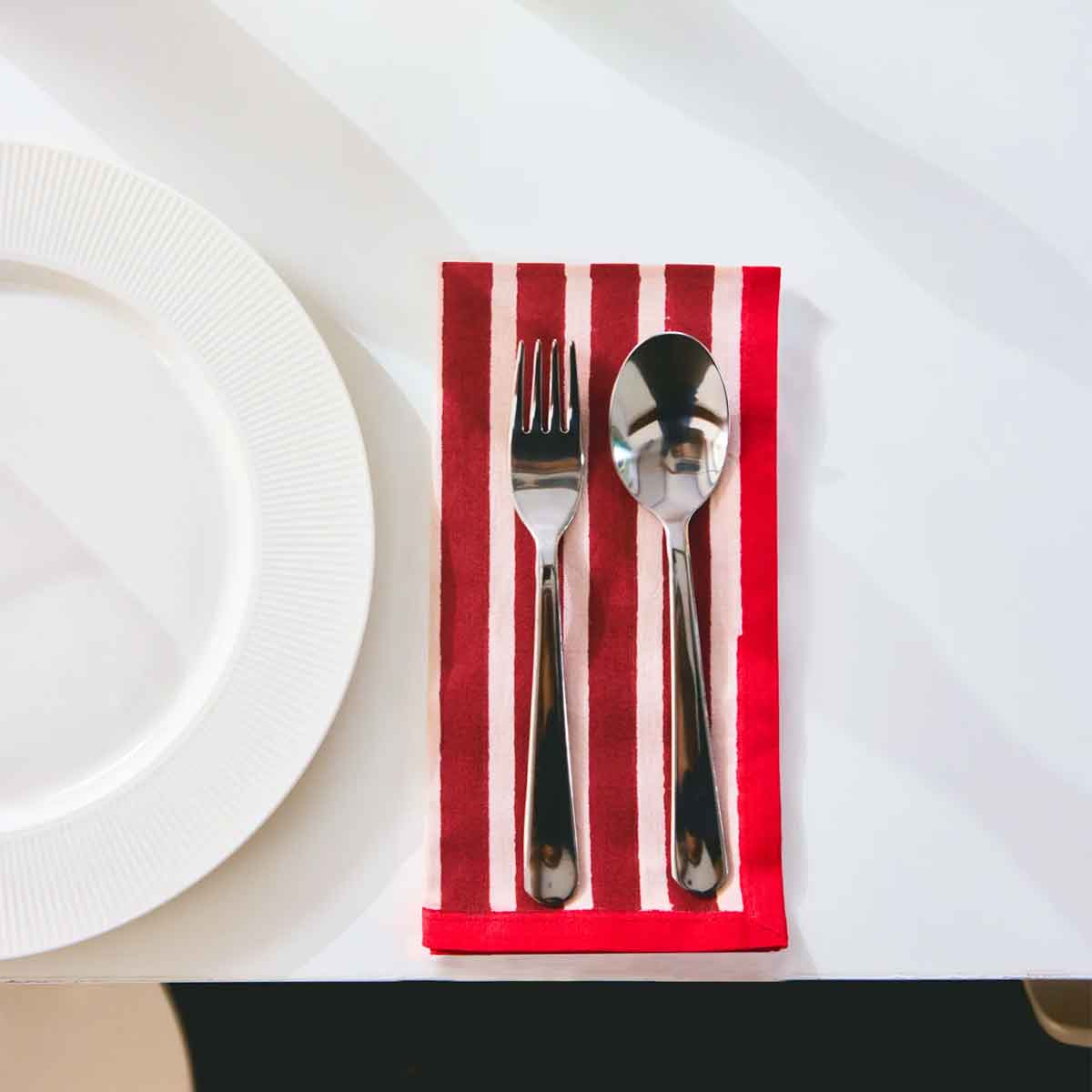Silver fork and spoon on a red and white striped napkin with a white plate in the background.