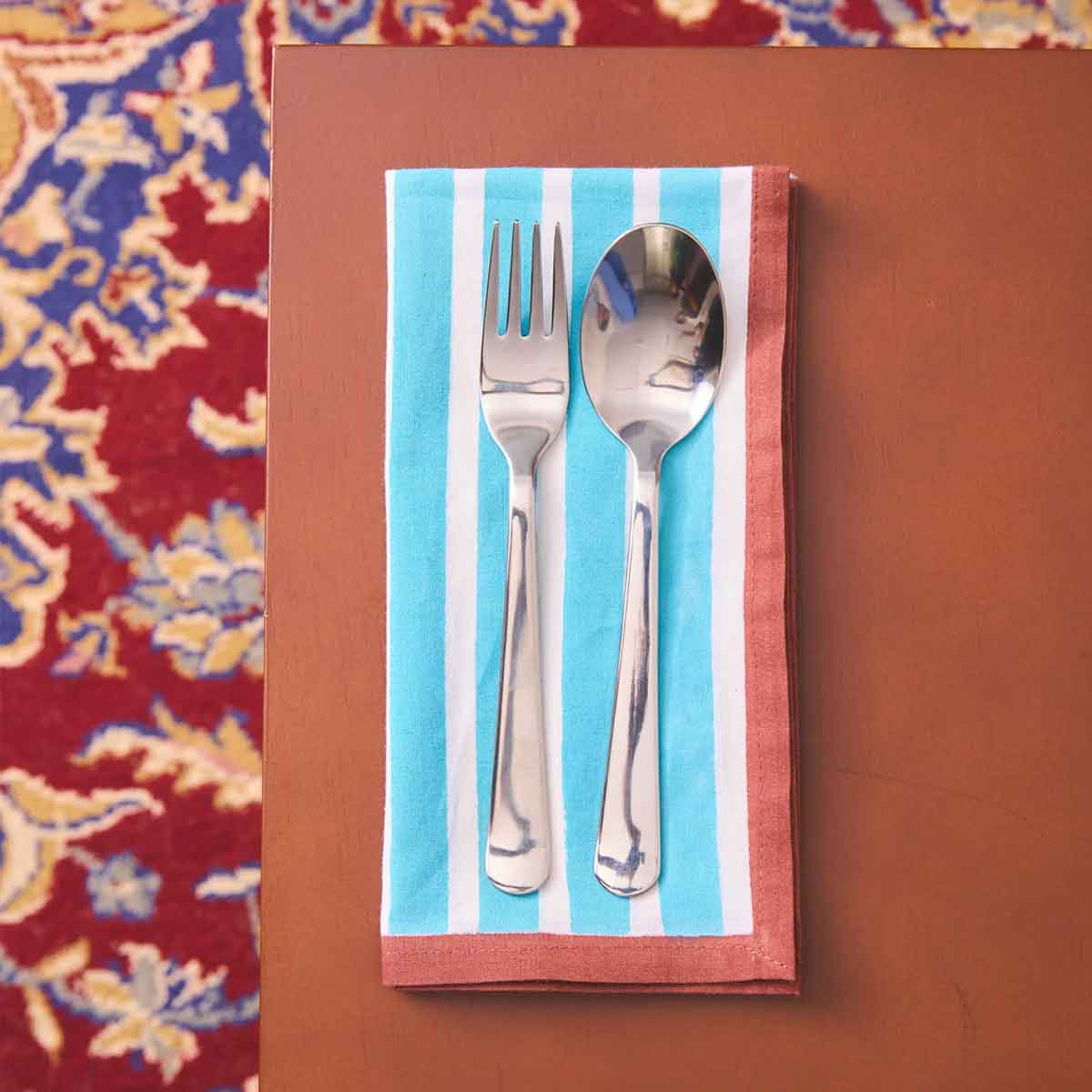 Silver fork and spoon on a striped napkin against a floral-patterned background